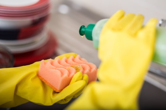 Cleaning dishware kitchen sink sponge washing dish. Close up of female hands in yellow protective rubber gloves washing