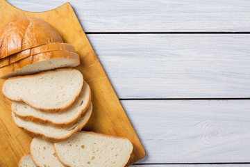 Fresh bread slices on cutting board against white wooden background. Top view