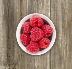 Raspberries in a white ceramic bowl. Ripe and tasty raspberries isolated on a wooden background. Top view.