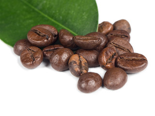 Naklejka premium Pile of coffee grains with green leaf over white isolated background.