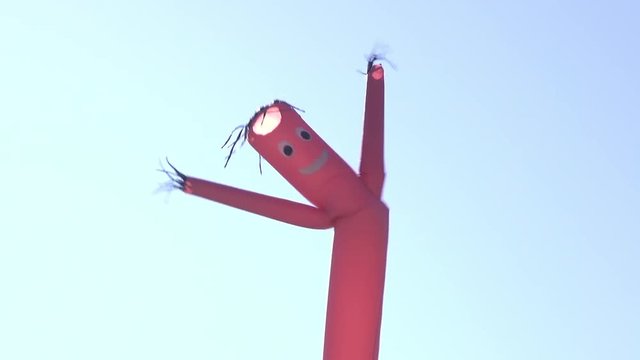 Super wiggly inflatable armed balloon man blowing in wind on blue sky attracting customers.
