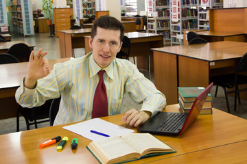 Young cheerful student or teacher in library shows ok gesture.