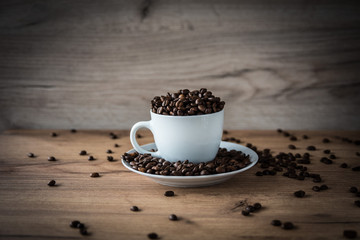 coffee cup filled by coffee beans on wooden background