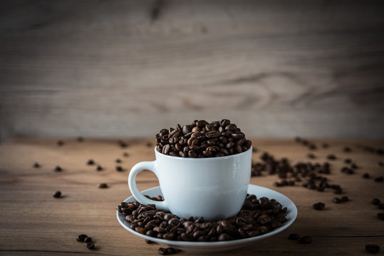 coffee cup filled by coffee beans on wooden background