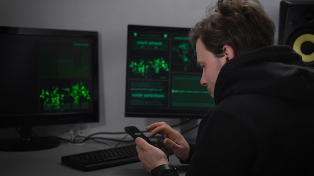 Adult male Hacker, with stubble on his face, wearing a black sports jacket sits in a secret bunker and makes cyber attacks. On your smartphone, he said the data