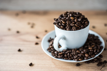 coffee cup filled by coffee beans on wooden background