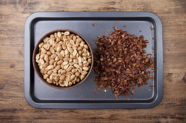 Fried peanuts in a clay bowl and husk on a baking sheet