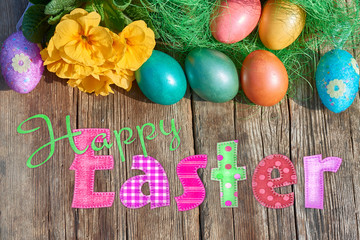 Easter eggs in nest on old wooden background with yellow flower and Text Happy Easter