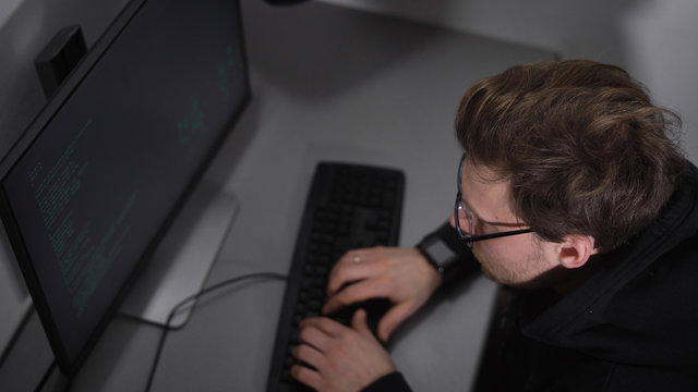 Underground Computer Room. A hacker using special software tries to crack the important information. A man in a dark jacket and glasses gathers information using the keyboard is very concentrated.