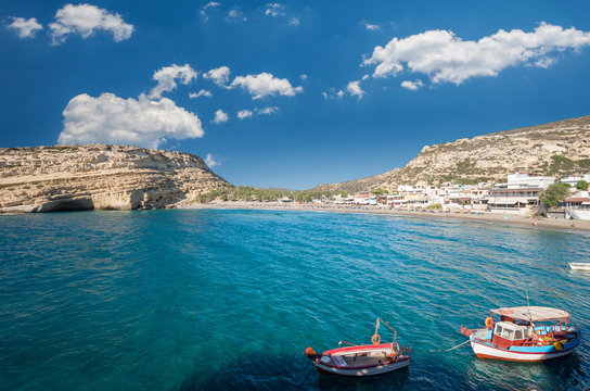 Matala beach on Crete island, Greece. There are two boats in the foreground and many caves near the beach.