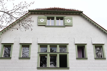 Hausfassade bedeckt mit weißen Schindel und grün eingefassten Fenstern
