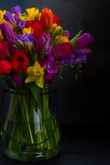 bouquet of bright spring flowers in vase on dark background close up