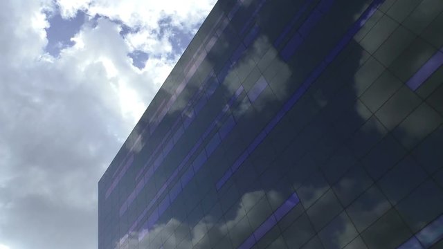 Reflection of the sky in a glass facade of a modern building. Floating clouds above contemporary architecture in a sunny day.