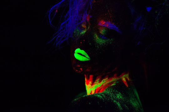 Beautiful extraterrestrial model woman with blue hair and green lips in neon light. It is close portrait of beautiful model with fluorescent make-up, Art design of female posing in UV with colorful