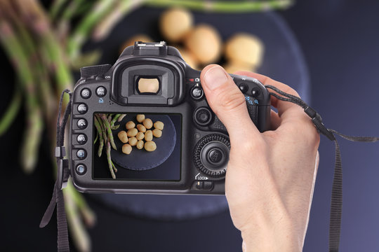 Male hand taking photo of new potatoes and Asparagus on black background with digital DSLR camera.