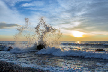 Big sea wave breaks against a stone at beautiful sunrise