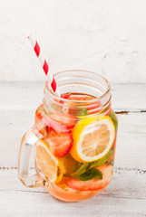 Infused detox diet refreshing water with strawberries and lemon. On white wooden table, in Mason Jar copy space vertical