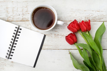 Red tulips, coffee cup and notebook over white wood table. Flat lay