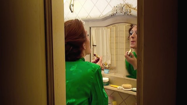 A harsh lady (woman in character) applying lipstick to her face in the bathroom. Funny comedy shot.
