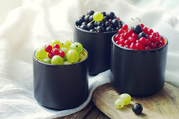 Fresh juicy berries of a gooseberry, black and red currant in cups. Summer harvest of berries