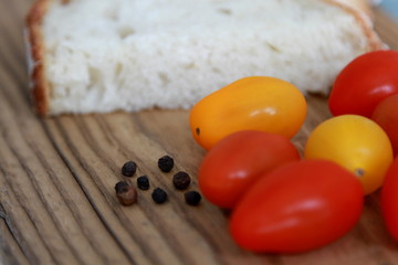 Brotscheibe mit farbigen Tomaten und schwarzen Pfefferkörnern auf Holztisch