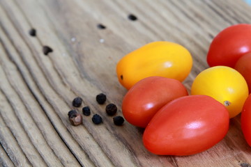 Farbige Tomaten mit schwarzen Pfefferkörnern auf Holztisch