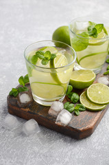 Cold refreshing summer drink with lime and mint in a glass on a grey concrete or stone background, selective focus, copy space.