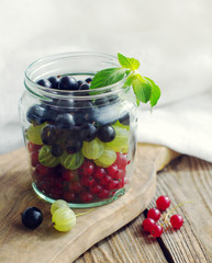 Fresh juicy berries of a gooseberry, black and red currant n a glass jar on a wooden board. Summer harvest of berries
