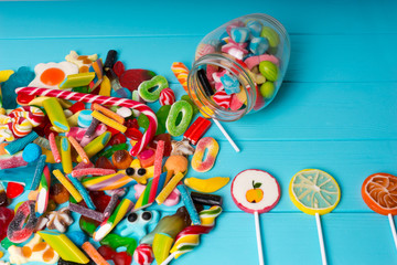 View from above on cattered candies and lollipops as fruits near glass can with chewing sweets