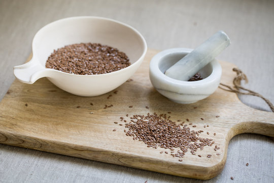 Flax seeds in bowl on wooden board on linen cloth background 