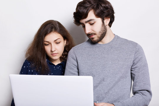 Modern technology and communication concept. A stylish bearded man and pretty woman watching video or browsing pictures on internet using free wi-fi on generic laptop. Selective focus