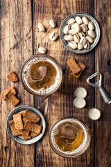 Two glasses of fresh beer and salty snacks on a brown wooden table, top view