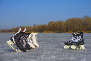 White figure skates and black hockey skates on the spring ice in sunny day