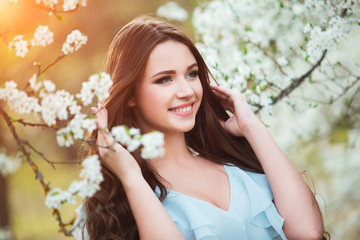 Fototapeta premium Happy beautiful young woman with long black healthy hair enjoy fresh flowers and sun light in blossom park at sunset.