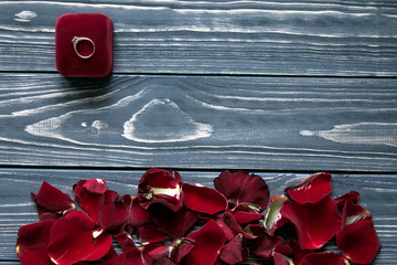 Petals of red roses in a circle and a red box with a ring on it. Gray wooden background.Space for text.