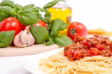 Spaghetti bolognese,some tomatoes, olive oil, basil, garlic, and raw pasta in the background