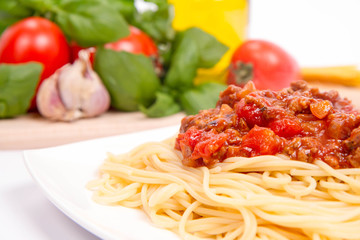 Spaghetti bolognese,some tomatoes, olive oil, basil, garlic, and raw pasta in the background