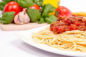 Spaghetti bolognese,some tomatoes, olive oil, basil, garlic, and raw pasta in the background