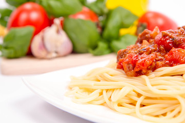 Spaghetti bolognese,some tomatoes, olive oil, basil, garlic, and raw pasta in the background