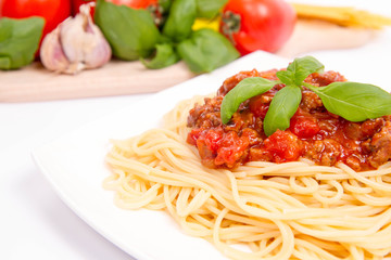 Spaghetti bolognese,some tomatoes, olive oil, basil, garlic, and raw pasta in the background
