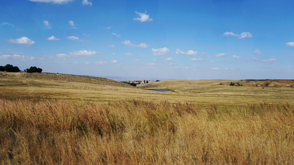 Fototapeta na wymiar Trockenes Land in Südafrika/Trockenes Land in Südafrika im Herbst, braune Wiesen und Felder, blauer Himmel mit weißen Wolken