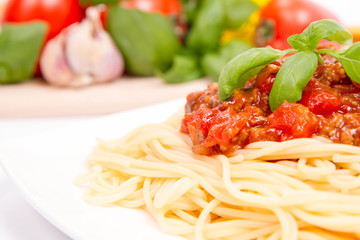Spaghetti bolognese,some tomatoes, olive oil, basil, garlic, and raw pasta in the background