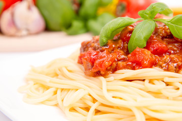 Spaghetti bolognese,some tomatoes, olive oil, basil, garlic, and raw pasta in the background