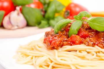 Spaghetti bolognese,some tomatoes, olive oil, basil, garlic, and raw pasta in the background