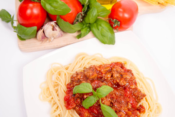 Spaghetti bolognese,some tomatoes, olive oil, basil, garlic, and raw pasta in the background