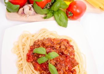 Spaghetti bolognese,some tomatoes, olive oil, basil, garlic, and raw pasta in the background