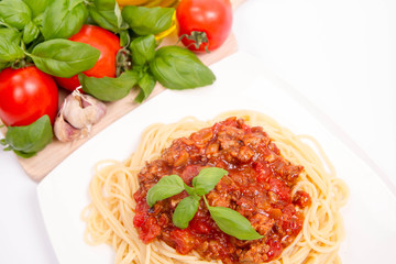 Spaghetti bolognese,some tomatoes, olive oil, basil, garlic, and raw pasta in the background