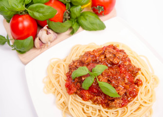 Spaghetti bolognese,some tomatoes, olive oil, basil, garlic, and raw pasta in the background