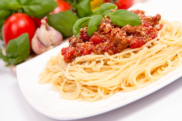 Spaghetti bolognese,some tomatoes, olive oil, basil, garlic, and raw pasta in the background