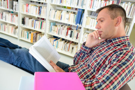 Man reading in library with feet on table